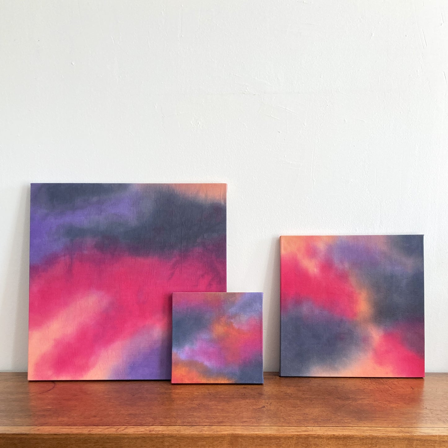 A grouping of three abstract cloud paintings in tones of pink, peach and gray.