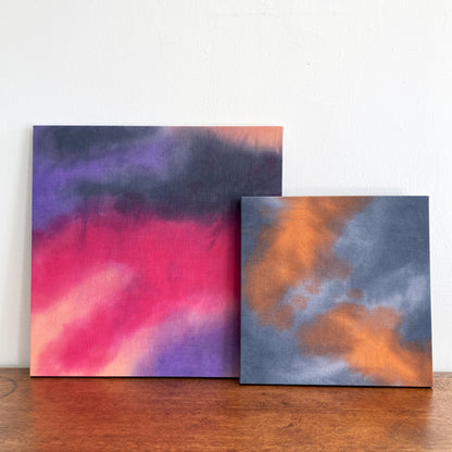 A grouping of two abstract cloud paintings in tones of pink, peach, blue and gray.