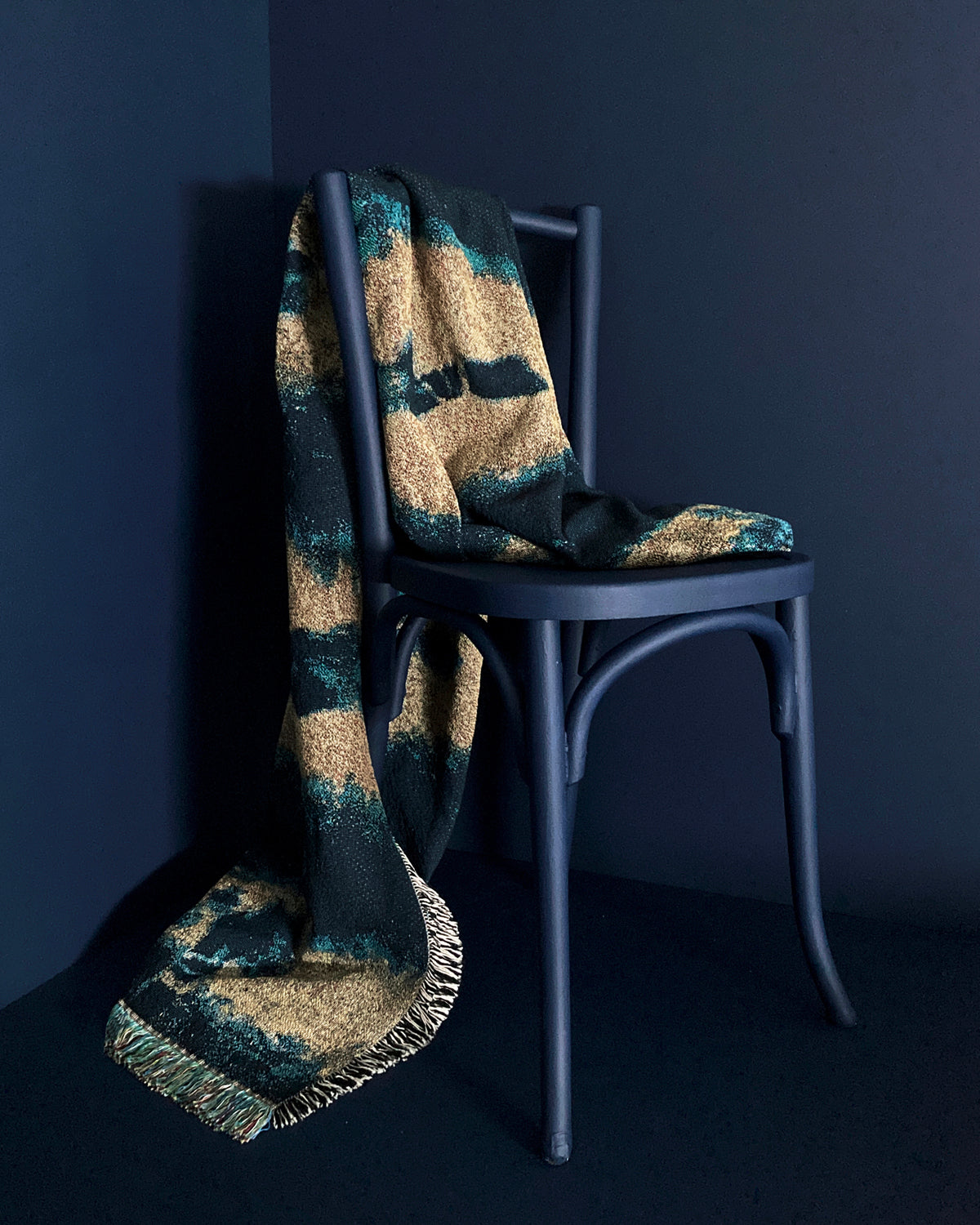 Draped over chair, gold yellow and indigo blue woven cotton throw blanket with fringed edges. 54 by 72 inches. Against navy background.